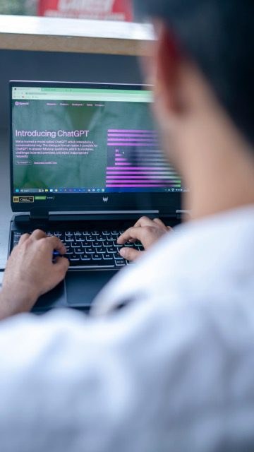 A person typing on a laptop with OpenAI's 'Introducing ChatGPT' page on screen.