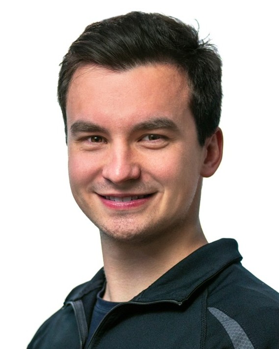 Justin Creasy, smiling, in a dark quarter-zip jacket against a white background.